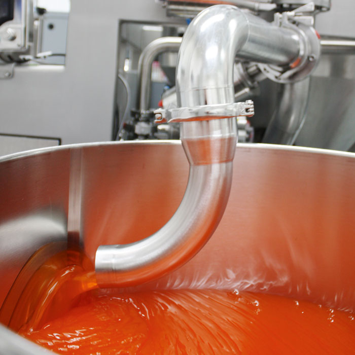 Ein großes Gefäß mit orangefarbener Pferdesalbe wird über ein großes Metallrohr befüllt.